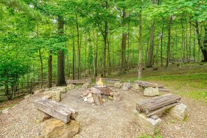 A campsite with a fire pit surrounded by rocks and logs, set in a forested area. - Lodge at Wildcat Hollow | Game Room, Hot Tub (Rockbridge)