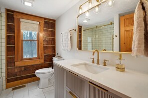 A bathroom with a wooden wall, a white toilet, a sink with a gold faucet, and a mirror with lights.