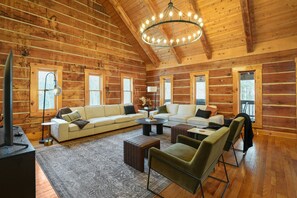 A log cabin interior with a large sofa, a coffee table, and a television.