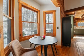 A cozy cabin interior with large windows, a dining table, and a kitchen area.