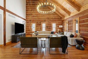 Ein geräumiges Wohnzimmer mit hoher Decke, Holzwänden, einem Chandelier, einem Flachbildfernseher und einer Sofagarnitur.