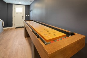 A shuffleboard table with numbered ends in a room with dark walls and a wooden floor. - Lodge at Wildcat Hollow | Game Room, Hot Tub (Rockbridge)