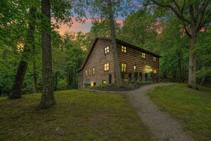 A rustic log cabin with a dirt path leading to it, surrounded by dense forest.