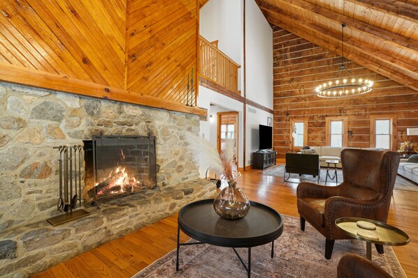 A spacious living room with a stone fireplace, wooden ceiling, and a cozy seating area.