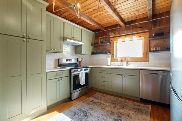 A kitchen with light green cabinets, a stainless steel stove, and a dishwasher.