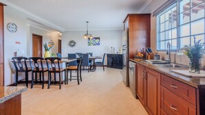 A modern kitchen with wooden cabinets, a large window, and a dining area with chairs and a table.