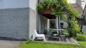 Una casa con porche cubierto, una mesa pequeña y sillas.