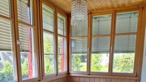 Una habitación con paneles de madera, una mesa y sillas blancas, ventanas amplias y una lámpara colgante.