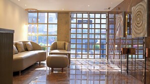 Una sala de estar moderna con un sofá, un reposapiés y una mesa de centro. Amplios ventanales con diseño de cuadrícula dejan entrar luz natural y ofrecen vistas de la ciudad.