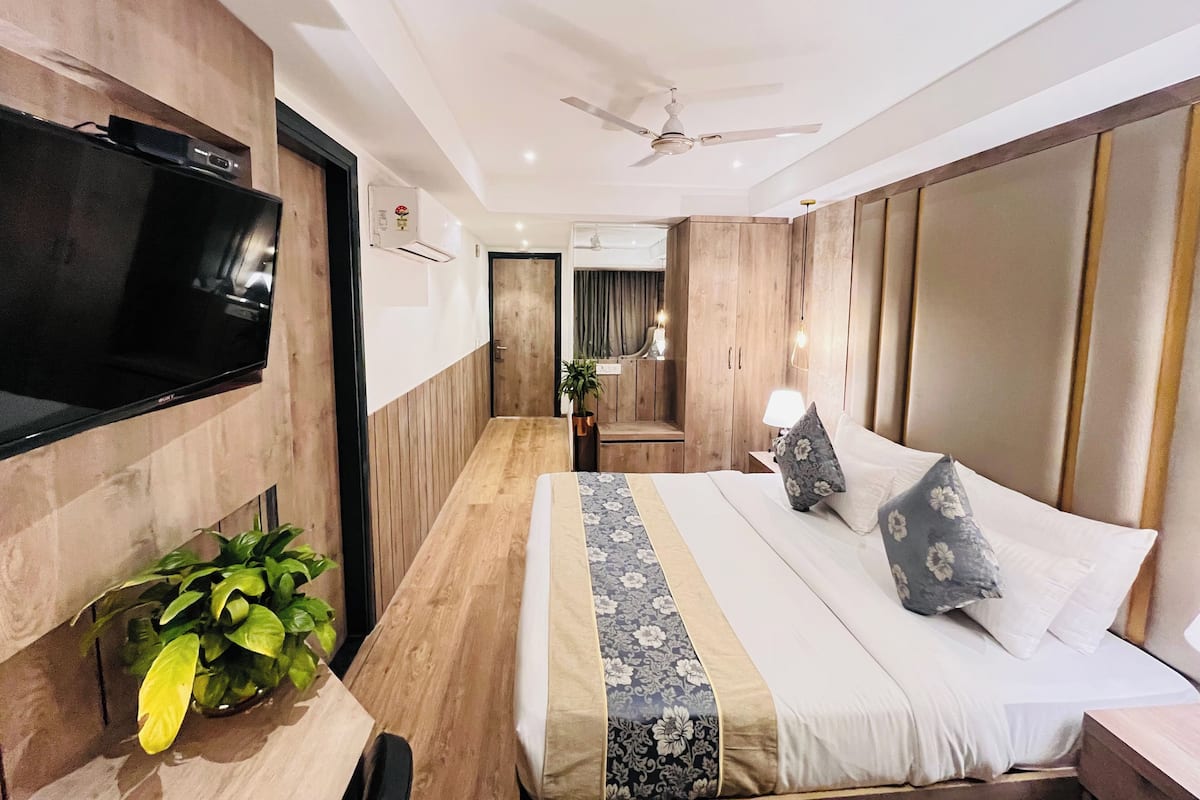Hotellihuone, jossa on sänky, televisio, kattotuuletin ja puinen vaatekaappi.