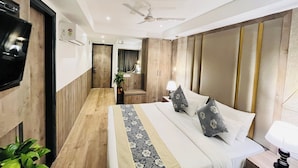 Una habitación de hotel con una cama, mesita de noche, lámpara y un televisor montado en la pared.