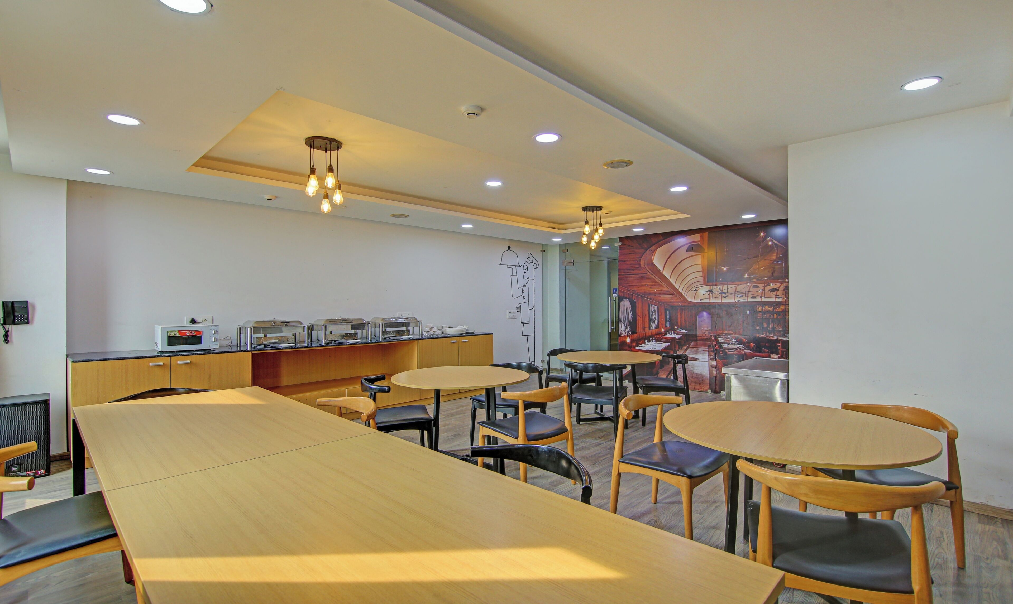 Un restaurante moderno con mesas y sillas de madera, un área de cocina con electrodomésticos y un mural en la pared.