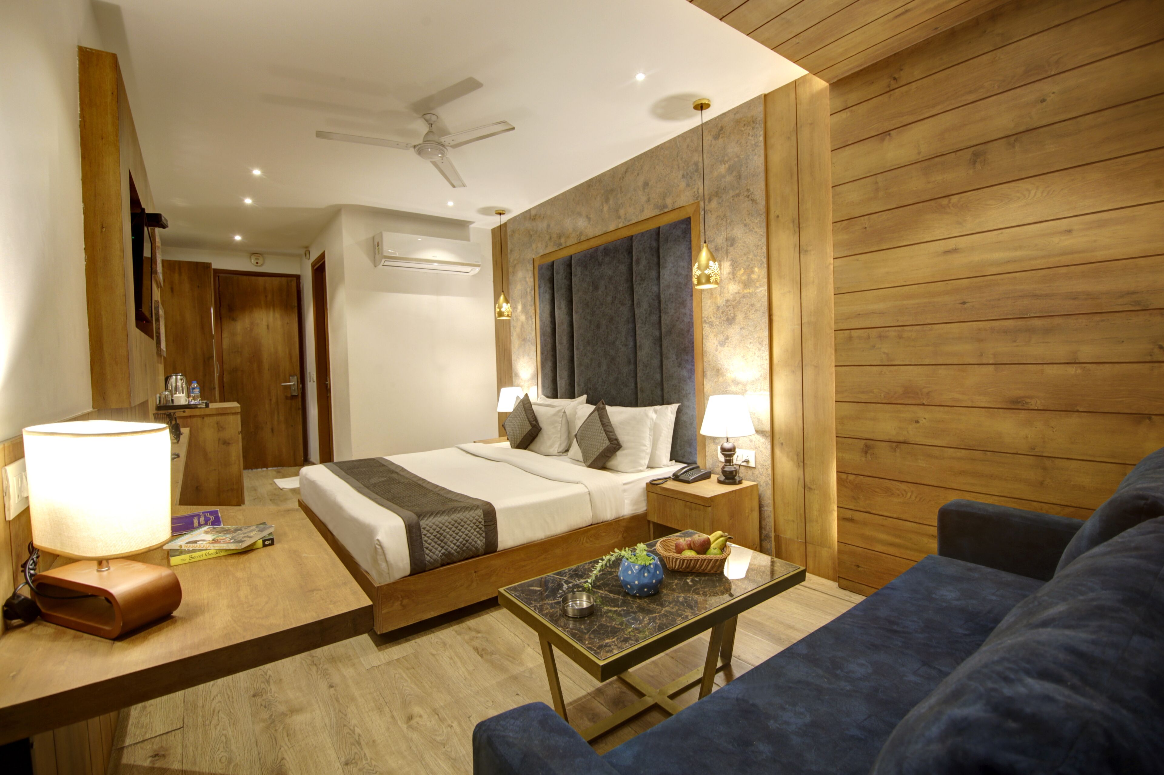 A hotel room with a bed, a desk, a chair, a ceiling fan, and wooden walls.