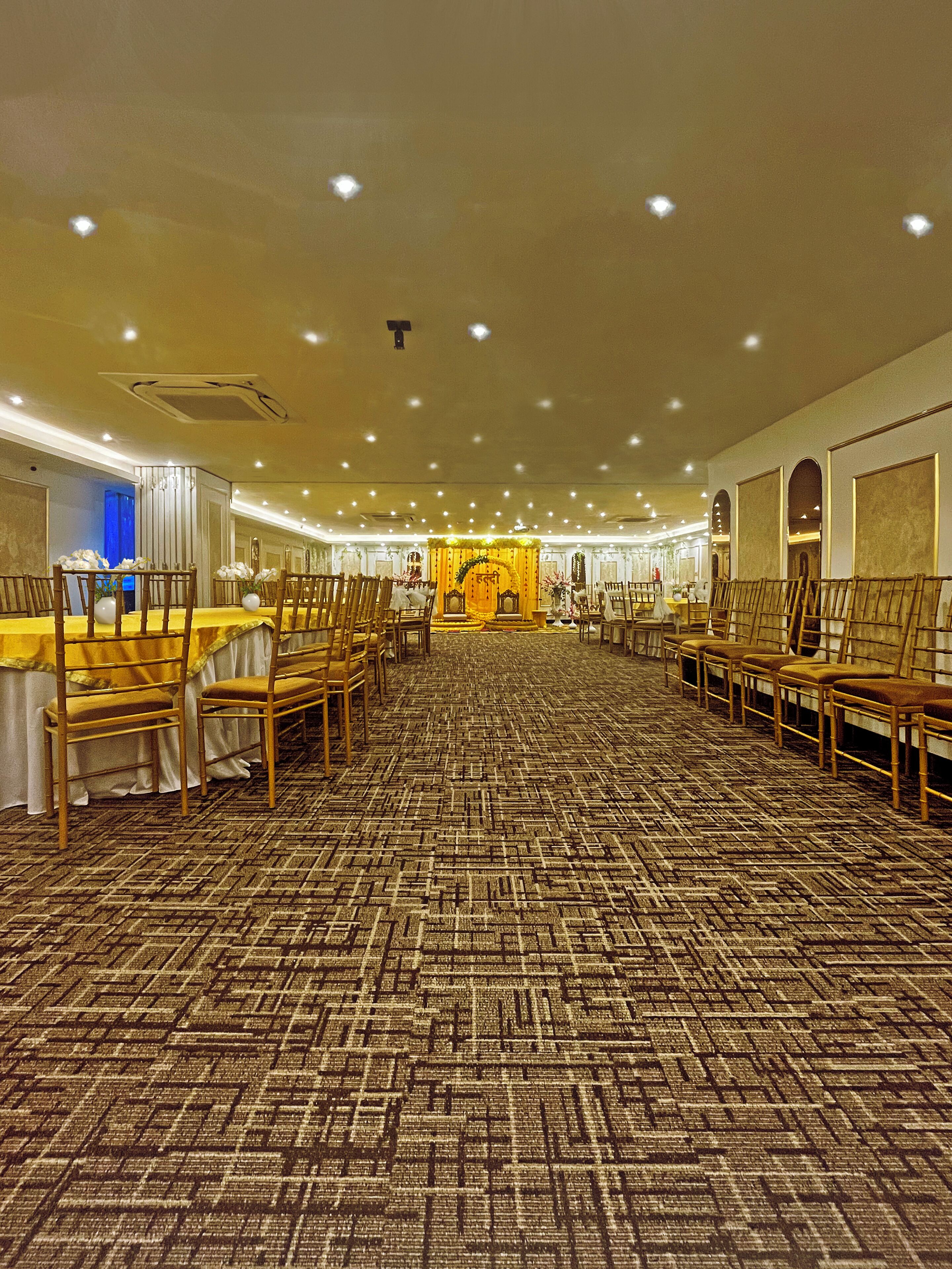 A banquet hall with rows of wooden chairs and tables, a patterned carpet, and a central decorative area.