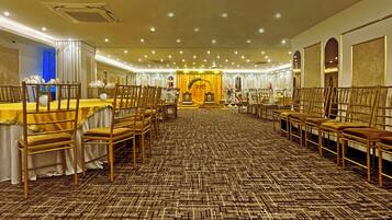 A banquet hall with rows of wooden chairs and tables, a patterned carpet, and a central decorative area.