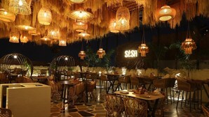 Un restaurante con mobiliario de mimbre, lámparas colgantes de mimbre y suelo de baldosas de piedra.