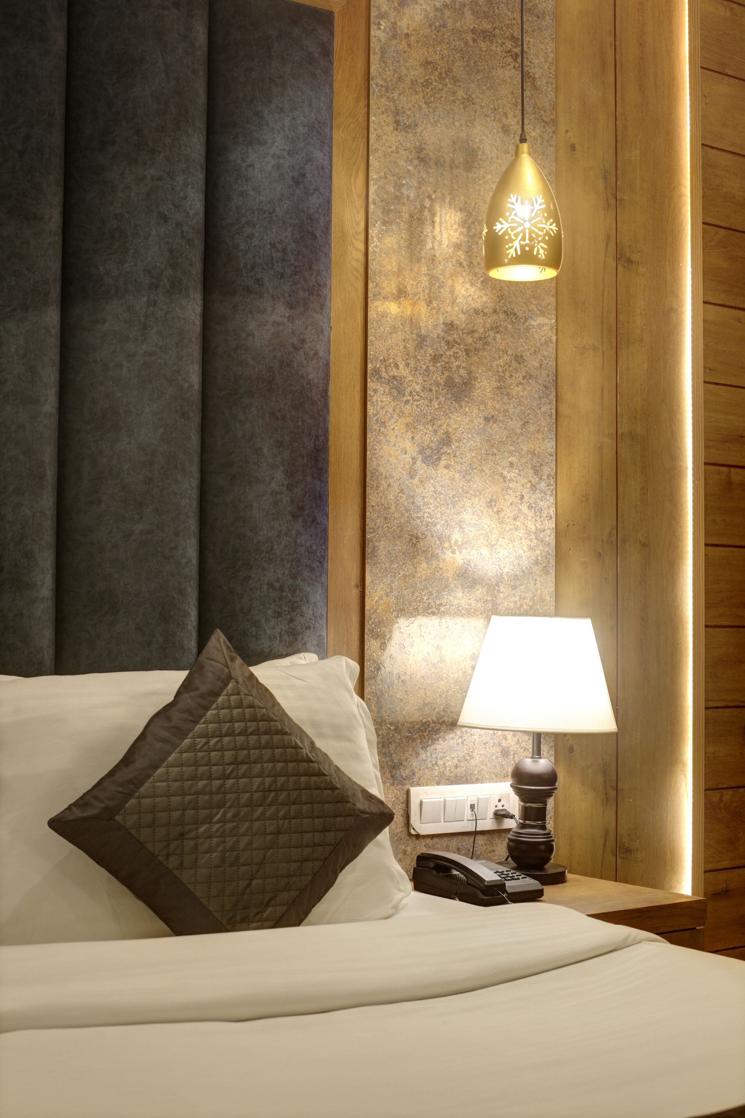 A hotel room with a bed, a bedside lamp, a telephone, and a hanging light fixture.