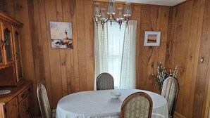 A dining room with a wooden paneled wall, a chandelier, a table with a white tablecloth, and chairs with herringbone-patterned upholstery.