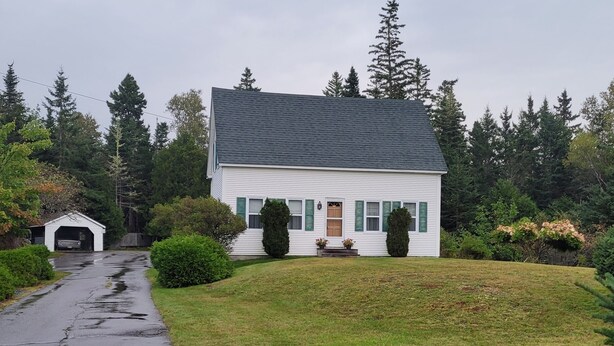 A white house with a dark roof, a front porch, and a driveway leading to a garage.