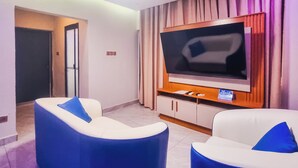 Una sala moderna con un televisor de pantalla plana montado en un mueble de madera, dos sofás azul y blanco y una puerta que da a otra habitación.
