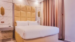 Un dormitorio moderno con una cama grande, una mesita de noche, una lámpara de pared y un ventanal con cortinas.