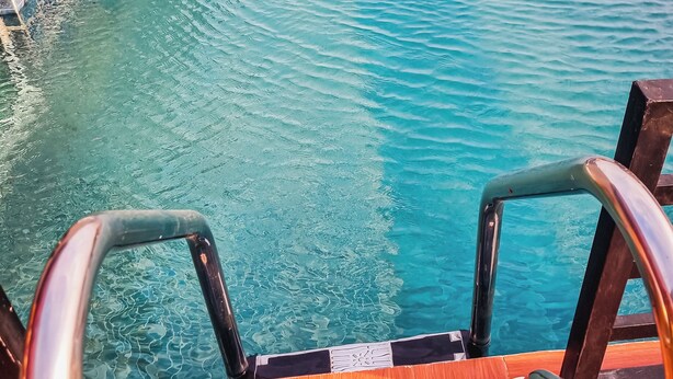 Piscina con agua cristalina, cubierta de madera y barandillas de metal.