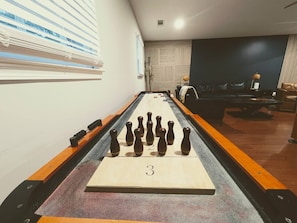 Une table de baby-foot dans une pièce avec un mur sombre, une fenêtre avec des stores et un canapé.