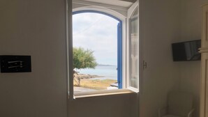 A room with a window offering a view of a beach and sea.