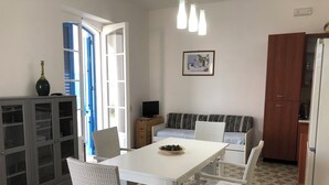 A dining area with a white table and chairs, a sofa, a cabinet, and a television.