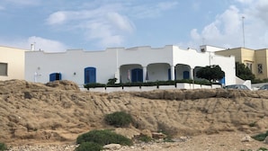 A white building with blue shutters and a sandy hill in the foreground.