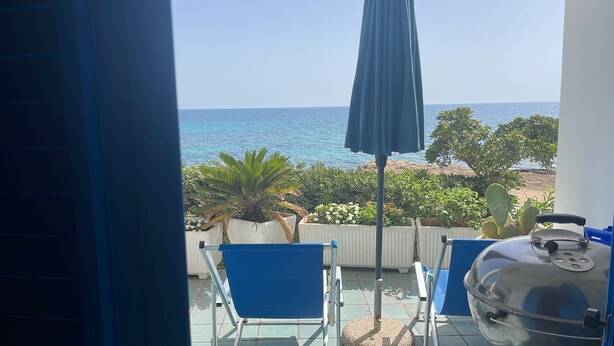 A balcony with a view of the sea, a grill, and blue chairs.