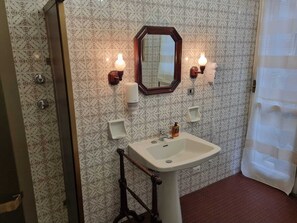 Un baño con baldosas estampadas, un lavamanos pedestal, un espejo e iluminación en la pared.