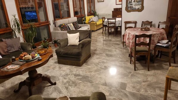 Una sala de estar con sofá, sillones, una mesa de comedor con sillas y un televisor sobre un mueble de madera.