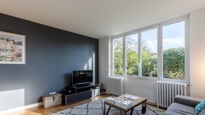 Ein modernes Wohnzimmer mit großem Fenster, einem Flachbildfernseher, einer Couch und einem Couchtisch.
