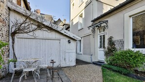 Ein schmales Innenhof mit einer weißen Holztür, einem Tisch mit Stühlen und einem Kiesweg.