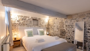 Ein Schlafzimmer mit Steingemäuer, einem Holzkopfende, einem Bett mit weißen Leinen und einem Nachttisch mit Lampe.