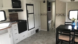 A compact kitchen with white cabinets, a microwave, a stove, and a small dining area with a table and chairs.