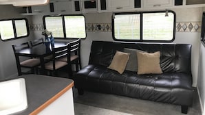 A compact RV interior with a dining area, a black leather couch with cushions, and a kitchen counter.