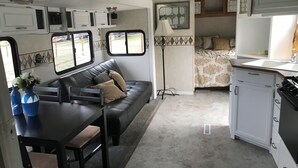 A compact RV interior with a kitchenette, a dining area, and a seating area with a sofa and table.