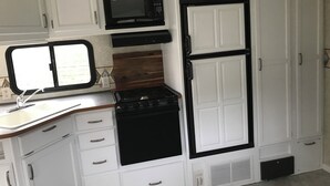 A compact kitchen with white cabinetry, a microwave, a stove, and a refrigerator.