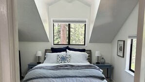 A bedroom with a sloped ceiling, a bed with striped bedding, two bedside tables with lamps, and a window with a view of trees. - Quiet 1 Bdrm walk to beach & trails.  Close to ski areas. (Kings Beach)