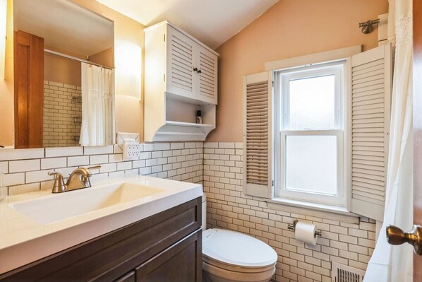 A bathroom with a white sink, dark wooden vanity, a toilet, and a window with shutters.