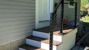 A house with a front porch, a set of wooden steps, and a black metal railing. - Coastal Private Guest Suite (Cohasset)
