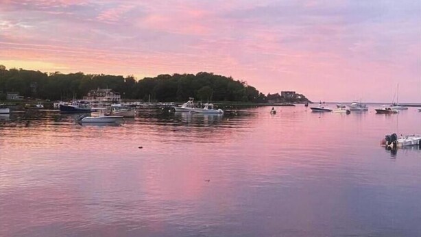 A marina with boats docked, calm water, and a shoreline with trees and buildings. - Coastal Private Guest Suite (Cohasset)