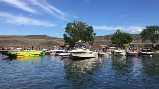 Un lago con varias embarcaciones amarradas, rodeado de árboles y colinas.