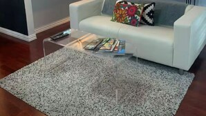 A living room with a white sofa, a coffee table, a kitchen area in the background, and a ceiling fan.