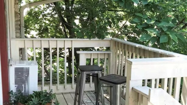 A wooden deck with a white railing, two metal barstools, and a potted plant.