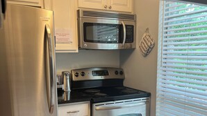 A compact kitchen with stainless steel appliances, including a refrigerator, microwave, stove, and oven. There are two sinks and a window with blinds.