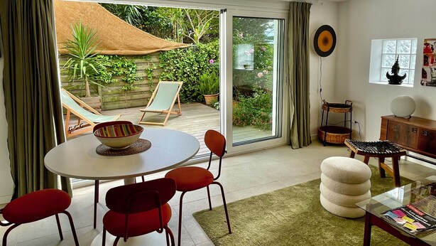 A room with a dining table, red chairs, a glass coffee table, a sofa, a small cabinet, and a view of a garden through a glass door. - 3-room apartment, 2 bedrooms, terrace ;Bibi area (Biarritz)