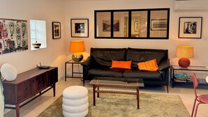 A modern living room with a black leather sofa, a round ottoman, a wooden coffee table, and a glass side table with a lamp. - 3-room apartment, 2 bedrooms, terrace ;Bibi area (Biarritz)